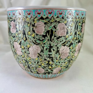 Puede incluir: Un macetero grande, redondo, de porcelana negra y blanca con un diseño floral. El macetero tiene flores rosas, hojas verdes y detalles amarillos. El borde del macetero está decorado con un borde turquesa y rosa.