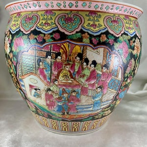 May include: A large, round, black and white porcelain planter with a colourful floral design and a scene of people in traditional Chinese clothing. The planter has a pink rim and a yellow base.