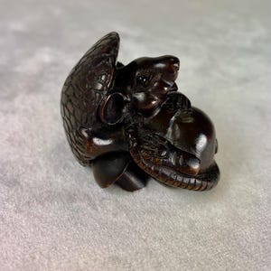 Puede incluir: Una escultura de madera marrón oscuro de una rata sentada sobre un caparazón de tortuga. La rata está tallada con detalle y tiene un aspecto realista.