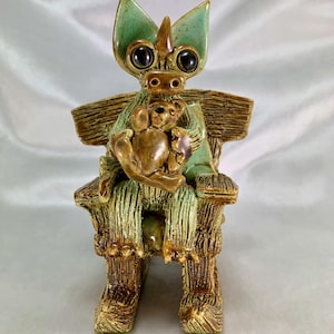 May include: A green and brown ceramic dragon figurine sitting in a rocking chair, holding a brown teddy bear.