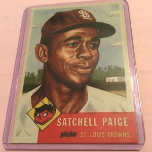 Könnte beinhalten: Eine Vintage-Baseballkarte mit einem Porträt von Satchel Paige, der eine braune Mütze mit weißem Logo trägt. Die Karte enthält eine kleine gelbe Rauten-Grafik mit einem Cartoon-Gesicht, den Namen SATCHEL PAIGE und den Text pitcher ST. LOUIS BROWNS.