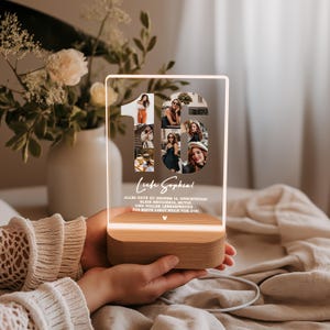 May include: A personalized LED night light with a wooden base. The light features the number "16" with several photos inside. The words "Liebe Sophia!" and a German message are also visible. The light is held in a person's hands.