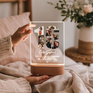May include: A personalized LED night light with a wooden base. The clear acrylic panel features the number "16" with photo cutouts and the name "Sophie". The light is illuminated, showcasing the photos and text.