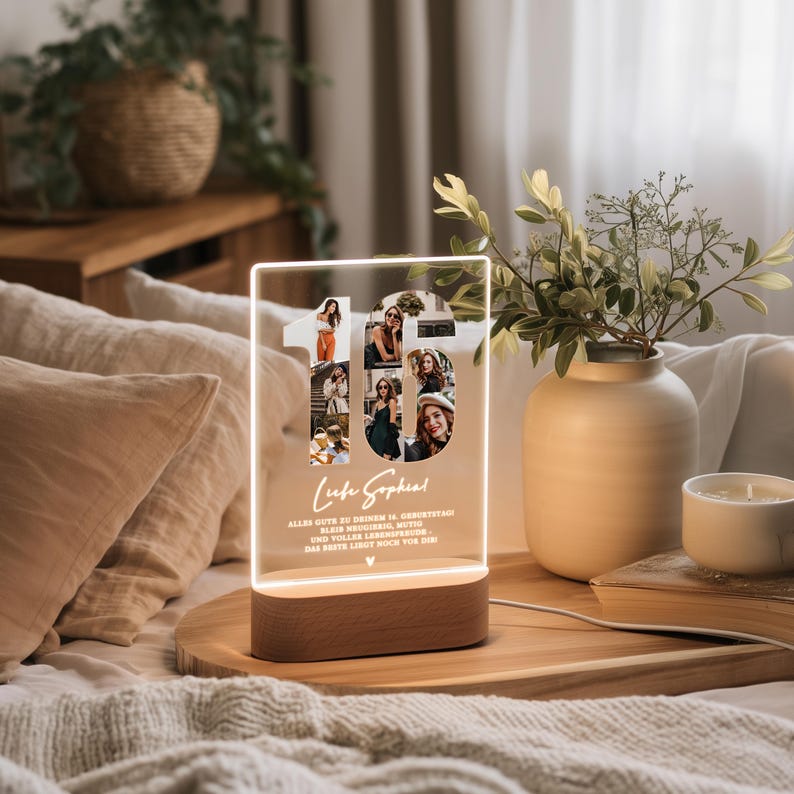 May include: A lighted acrylic photo display in the shape of the number 16, with multiple photos inside. The base is a brown wooden rectangle. Text includes a name and a birthday message. The display is on a wooden tray.