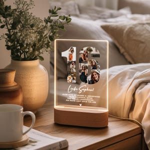 May include: A personalized LED night light with a wooden base. The clear acrylic panel features a collage of photos within the number "16" and includes text. The light is on a wooden nightstand next to a vase with greenery.
