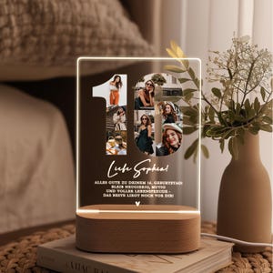 May include: A personalized LED night light with a wooden base. The light features a collage of photos forming the number 16, with text that reads "Liebe Sophia!" and a birthday message. The light is on a stack of books.