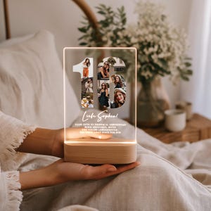 May include: A clear acrylic LED lamp with the number "16" filled with photos. The lamp has a wooden base and the text "Liebe Sophia!" and other text in German. The lamp is lit with a warm glow.