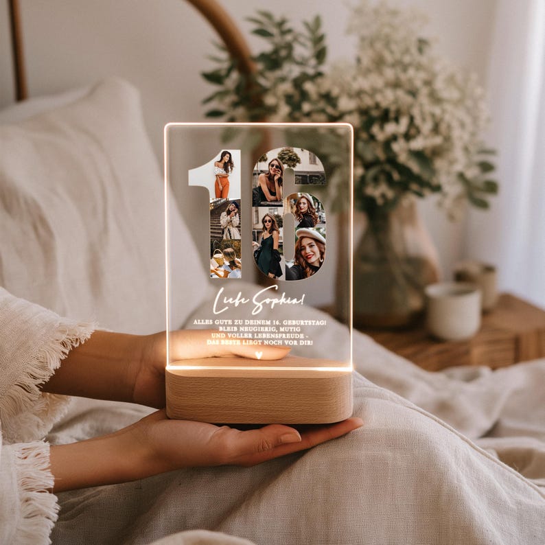May include: A clear acrylic LED lamp with the number "16" filled with photos. The lamp has a wooden base and the text "Liebe Sophia!" and other text in German. The lamp is lit with a warm glow.
