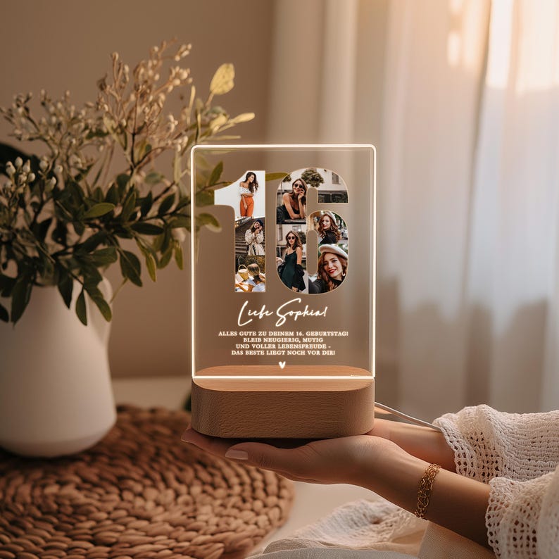 May include: A personalized LED night light with a wooden base. The clear acrylic panel features the number 16 filled with photos and the text "Liebe Sophia". The light is held in a person's hands.