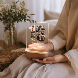 May include: A personalized LED night light with a wooden base. The clear acrylic panel features the number "16" filled with photos and the name "Luka Sophia!" in script. The light is on, illuminating the photos.