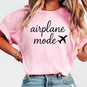 K&ouml;nnte beinhalten: Hellrosa T-Shirt mit dem schwarzen Schriftzug "airplane mode" und einer kleinen Flugzeug-Grafik. Das Shirt hat hochgekrempelte &Auml;rmel und eine l&auml;ssige Passform.