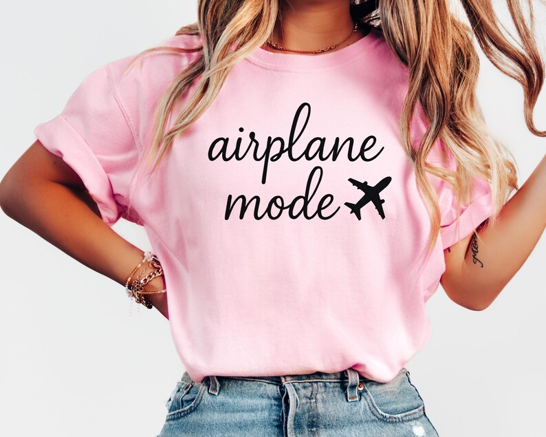 K&ouml;nnte beinhalten: Hellrosa T-Shirt mit dem schwarzen Schriftzug "airplane mode" und einer kleinen Flugzeug-Grafik. Das Shirt hat hochgekrempelte &Auml;rmel und eine l&auml;ssige Passform.
