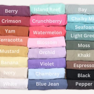 K&ouml;nnte beinhalten: Gefaltete T-Shirts in verschiedenen Farben, jeweils mit einem Farbnamen versehen. Farben sind Berry, Crimson, Yam, Terracotta, Mustard, Banana, Ivory, White, Island Reef, Crunchberry, Watermelon, Blossom, Orchid, Violet, Chambray und Blue Jean.