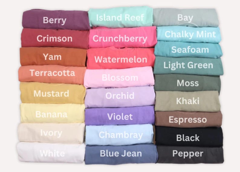 K&ouml;nnte beinhalten: Gefaltete T-Shirts in verschiedenen Farben, jeweils mit einem Farbnamen versehen. Farben sind Berry, Crimson, Yam, Terracotta, Mustard, Banana, Ivory, White, Island Reef, Crunchberry, Watermelon, Blossom, Orchid, Violet, Chambray und Blue Jean.