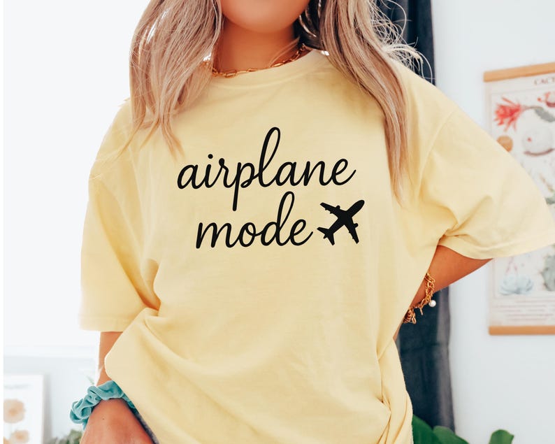 K&ouml;nnte beinhalten: Hellgelbes T-Shirt mit dem Schriftzug "airplane mode" in schwarzer Schrift und einer kleinen Flugzeuggrafik. Das Shirt hat eine lockere Passform und kurze &Auml;rmel.