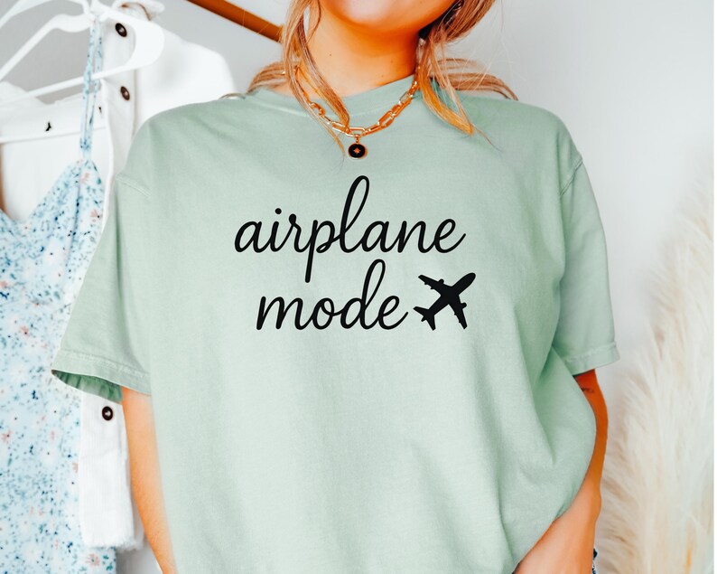 K&ouml;nnte beinhalten: Hellgr&uuml;nes T-Shirt mit dem schwarzen Schriftzug "airplane mode" und einer schwarzen Flugzeug-Grafik. Das Shirt hat einen l&auml;ssigen Stil.