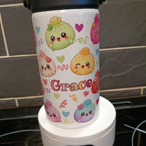 May include: A white insulated tumbler with a black lid and handle, featuring a colourful pattern of cartoon dumplings with faces, hearts, and squiggly lines. The name Grace is printed in the centre in a stylised, multi-coloured font.