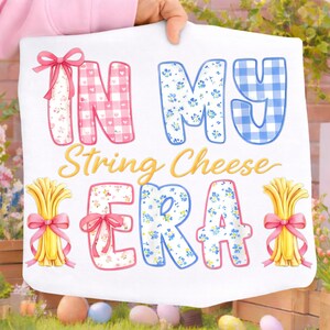 May include: White fabric featuring the phrase "IN MY String Cheese ERA". The text uses a mix of fonts and patterns, including gingham and floral designs. Illustrations of wheat bundles with pink bows are also present.