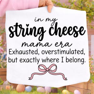 May include: White rectangular pillowcase with the text "in my string cheese mama era Exhausted, overstimulated, but exactly where I belong." The text is in black script font with a pink bow illustration.