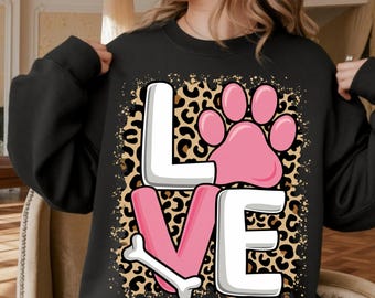 May include: Black sweatshirt with the word "LOVE" in a playful design. The "L" and "VE" are white, the "O" is a pink paw print, and the "V" is pink with a bone. The background has a leopard print.