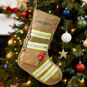 Könnte beinhalten: Beigefarbener Weihnachtsstrumpf mit reflektierenden gelben Streifen und dem Aufdruck "LIAM SMITH". Ein roter Hydrantenanhänger hängt an dem Strumpf, der im Feuerwehr-Thema dekoriert ist.