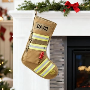 May include: A tan Christmas stocking with the name "DAVID" in black. It features reflective yellow and silver stripes, a small pocket, and a red fire hydrant charm. The stocking hangs from a white mantelpiece decorated with greenery and a red bow.