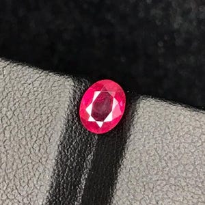 May include: A vibrant red oval-cut gemstone, likely a ruby, rests on a textured black surface. The gemstone's facets catch the light, displaying a bright, internal pattern. The overall presentation suggests a focus on jewelry or precious stones.