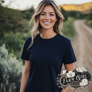 Könnte beinhalten: Eine Frau trägt ein dunkelblaues T-Shirt mit einem floralen Design in der rechten unteren Ecke. Das Design zeigt den Text "Farm Girl Digitals Mockups & Graphics".