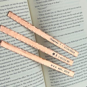 Peut inclure: Marque-pages en cuivre avec une texture martelée, posés sur un livre ouvert. Chaque marque-page porte l'inscription : "Chapter 7 - 2/14/2019", "I still do", et "m & s est. 2019".