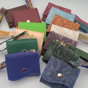 Cartera de vinilo/corcho de tres pliegues para mujer, disponible en varios colores. Ranuras transparentes para DNI y tres tarjetas, bolsillos para efectivo y cremallera con cierre a presión y correa para la muñeca.