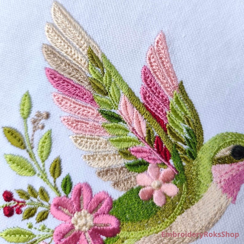 Floral hummingbird machine embroidery design with pink flowers, green leaves, cream feathers and botanical branches.