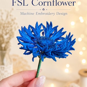 Peut inclure: Un bleuet d'un bleu éclatant réalisé en broderie machine, avec un travail de fil complexe et une tige verte. Le texte FSL Cornflower Machine Embroidery Design est affiché au-dessus de la fleur dans une police serif bleu foncé.