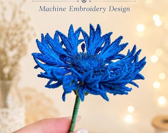 May include: A vibrant blue cornflower created as a machine embroidery design, featuring intricate thread work and a green stem. The text FSL Cornflower Machine Embroidery Design is displayed above the flower in a dark blue serif font.