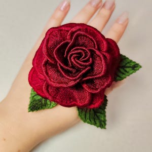 Red freestanding lace rose embroidery held in hand to show scale, texture, and 3D layered flower shape.