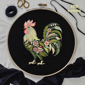 May include: Embroidered rooster design on black fabric in a hoop. The rooster is green, yellow, and pink with floral details.