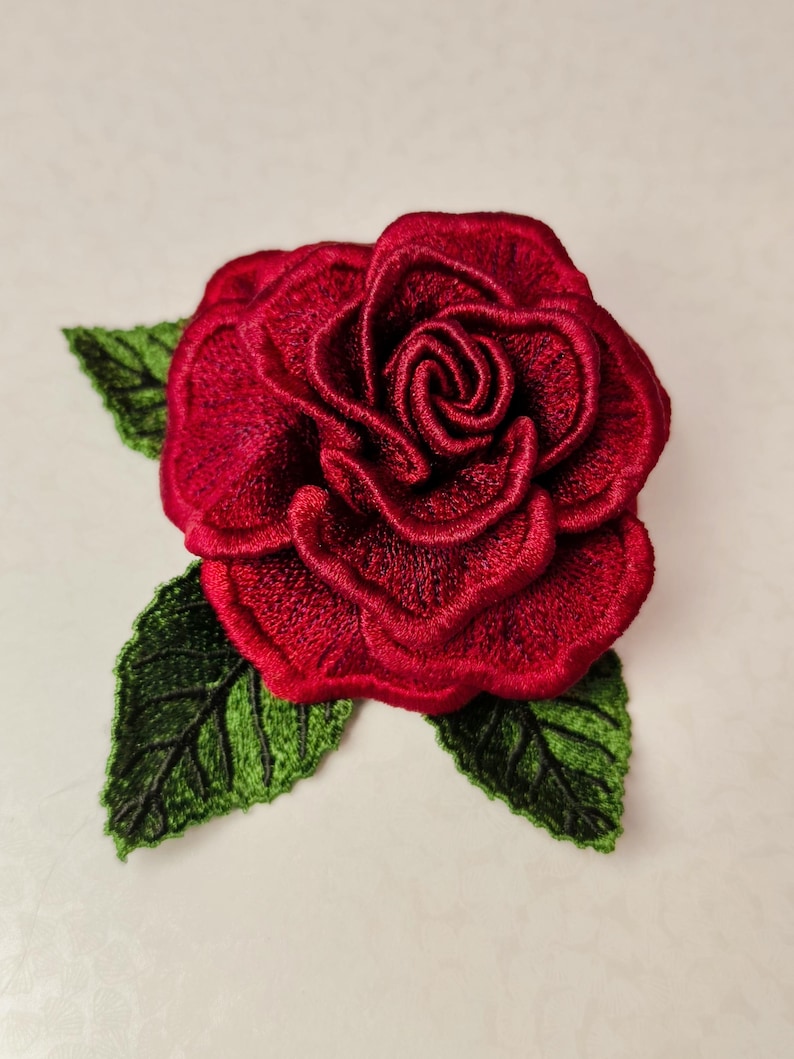 Red 3D FSL rose machine embroidery design with layered lace petals and green freestanding lace leaves.