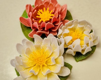 May include: Three embroidered water lily patches featuring layered petals in shades of coral and white, each with a bright yellow center. The flowers are attached to green circular lily pad bases with detailed stitching throughout the design.