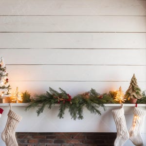 Peut inclure: Un manteau de cheminée de Noël décoré d'une guirlande de branches de conifères, de baies rouges et de petites lumières. Deux bas en tricot de câble blancs sont suspendus à la cheminée en briques. Des sapins de Noël miniatures et des lumières complètent le décor.