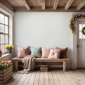May include: A wooden bench with a light brown finish and a woven throw blanket sits in a room with a white wall and a wooden ceiling. The bench is decorated with five pillows in shades of pink, green, and beige. A small wooden box sits in front of the bench, and a wreath of yellow flowers hangs on the wall.
