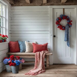 May include: A rustic bench with red, blue, and cream-colored pillows and a fringed throw blanket. A wreath of red and blue flowers hangs on a white door. Two galvanized buckets hold red, white, and blue flowers and American flags.
