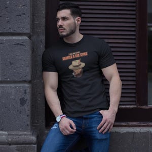May include: Black t-shirt with the text "A Real Man Knows Carries A Big Stick" above a cartoon image of a man wearing a hat and smoking a cigar. The shirt is paired with blue jeans.