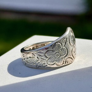 Könnte beinhalten: Ein silberner Ring mit einem floralen Design. Der Ring ist aus einem Löffel gefertigt und hat eine gebogene Form.