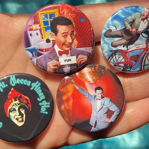 May include: Four round pinback buttons featuring images of a man in a suit, a man on a bicycle, a man with a turban, and a man with a dog. The buttons have a black background with white text that reads "Mecca Lecca Hi. Mecca Honey Hot!" on one button and "FUN" on another button.