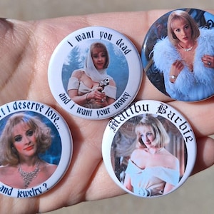 Op de afbeelding: Vier ronde buttons met afbeeldingen van een vrouw. Eén button heeft de tekst "I want you dead and I want your money". Een andere zegt "don't I deserve love... and jewelry?" De andere twee buttons hebben de tekst "Malibu Barbie".