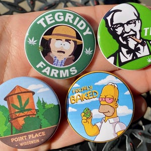 Könnte beinhalten: Vier runde grüne, blaue und gelbe Knöpfe mit Comicbildern. Der erste Knopf hat einen grünen Hintergrund mit einer Comicfigur, die einen Hut trägt und den Text "Tegridy Farms". Der zweite Knopf hat einen grünen Hintergrund mit einer Comicfigur, die ein weißes Hemd trägt und den Text "THC". Der dritte Knopf hat einen blauen Hintergrund mit einer Comicfigur, die ein grünes Objekt hält und den Text "Freshly Baked". Der vierte Knopf hat einen blauen Hintergrund mit einer Comicfigur und den Text "Point Place - Wisconsin".