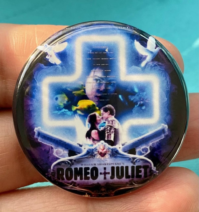 May include: A round button with a blue and purple background featuring a white cross with a couple in the center. The couple is standing in front of a blue and purple background with fish and doves. The text "ROMEO + JULIET" is at the bottom of the button.