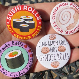 Puede incluir: Cuatro botones redondos con diferentes diseños. Cada botón tiene un fondo blanco con un gráfico colorido y texto. El texto en los botones dice "Sushi Rolls Not Gender Roles", "Cinnamon Rolls Not Gender Roles", "Sushi Rolls Not Gender Roles", y "Cinnamon Rolls Not Gender Roles".