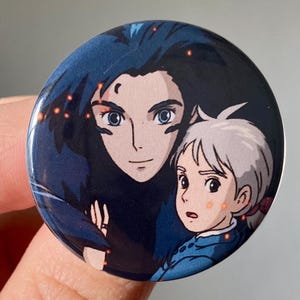 May include: A round button featuring a cartoon image of two characters from the animated film "Howl's Moving Castle". The characters are a young girl with white hair and a man with dark blue hair. The background is a dark blue with orange sparks.