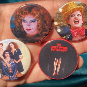 Peut inclure: Quatre badges ronds en forme de bouton représentant des personnages du film The Rocky Horror Picture Show. Les badges sont rouges, noirs et blancs avec des images du Dr. Frank-N-Furter, de Columbia et de Brad et Janet.