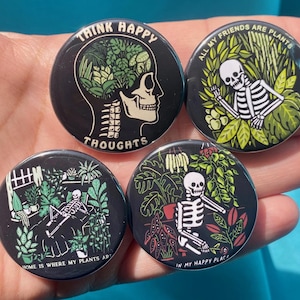 May include: Four round black and white buttons with green plant and skeleton illustrations. The buttons feature the text "Think Happy Thoughts", "All My Friends Are Plants", "Home Is Where My Plants Are", and "In My Happy Place".